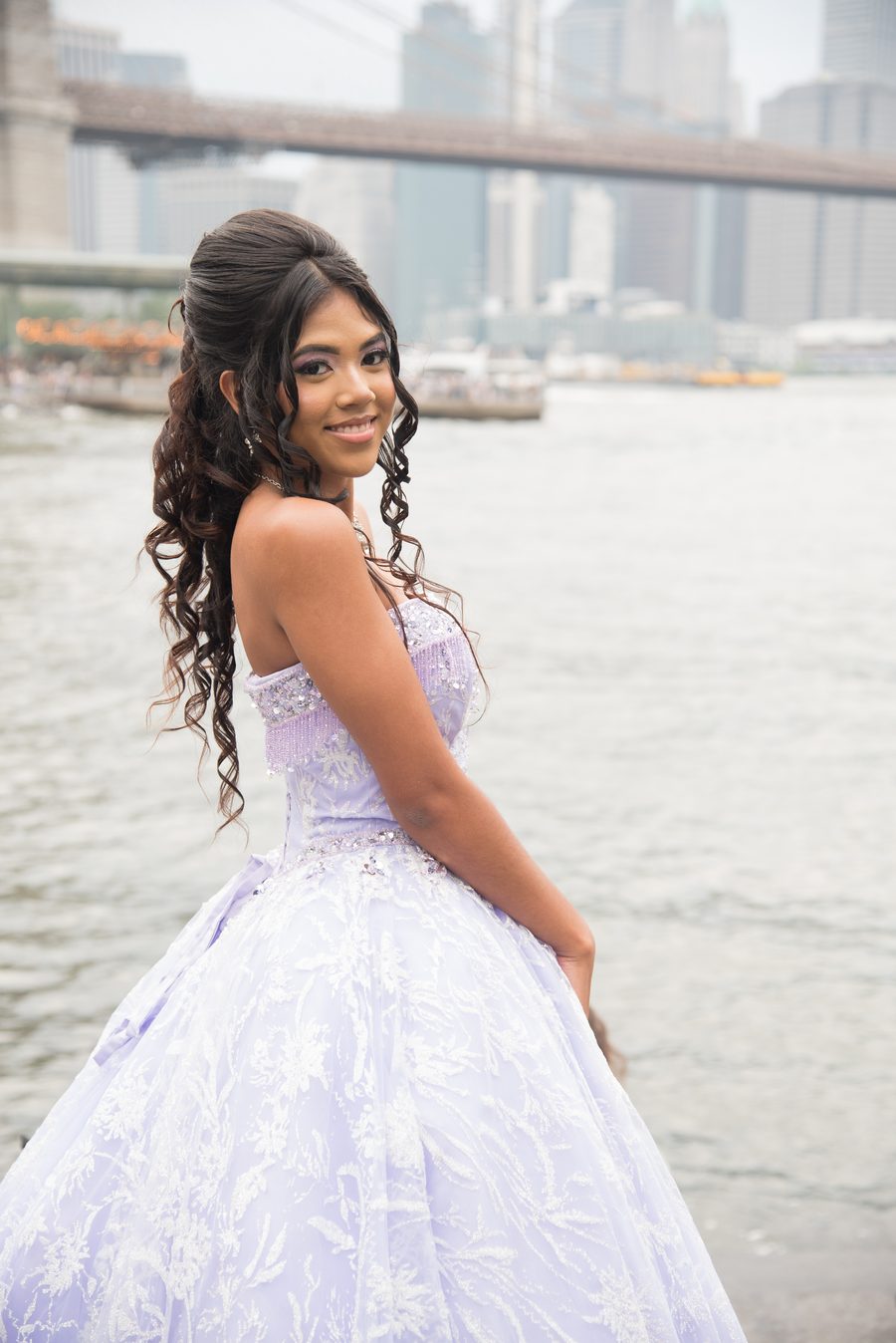 Quinceañera in a lilac gown smiling by the Brooklyn Bridge
