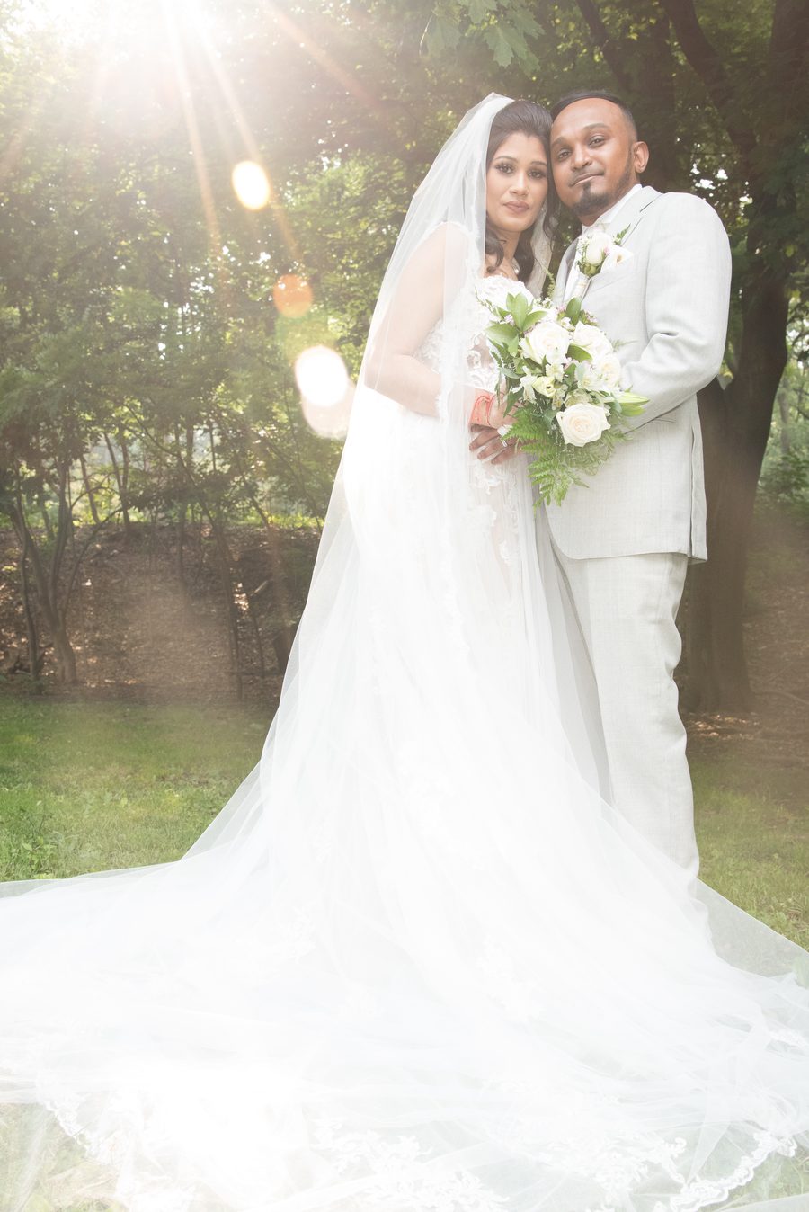 Bride and groom with a white rose bouquet beneath golden sun rays