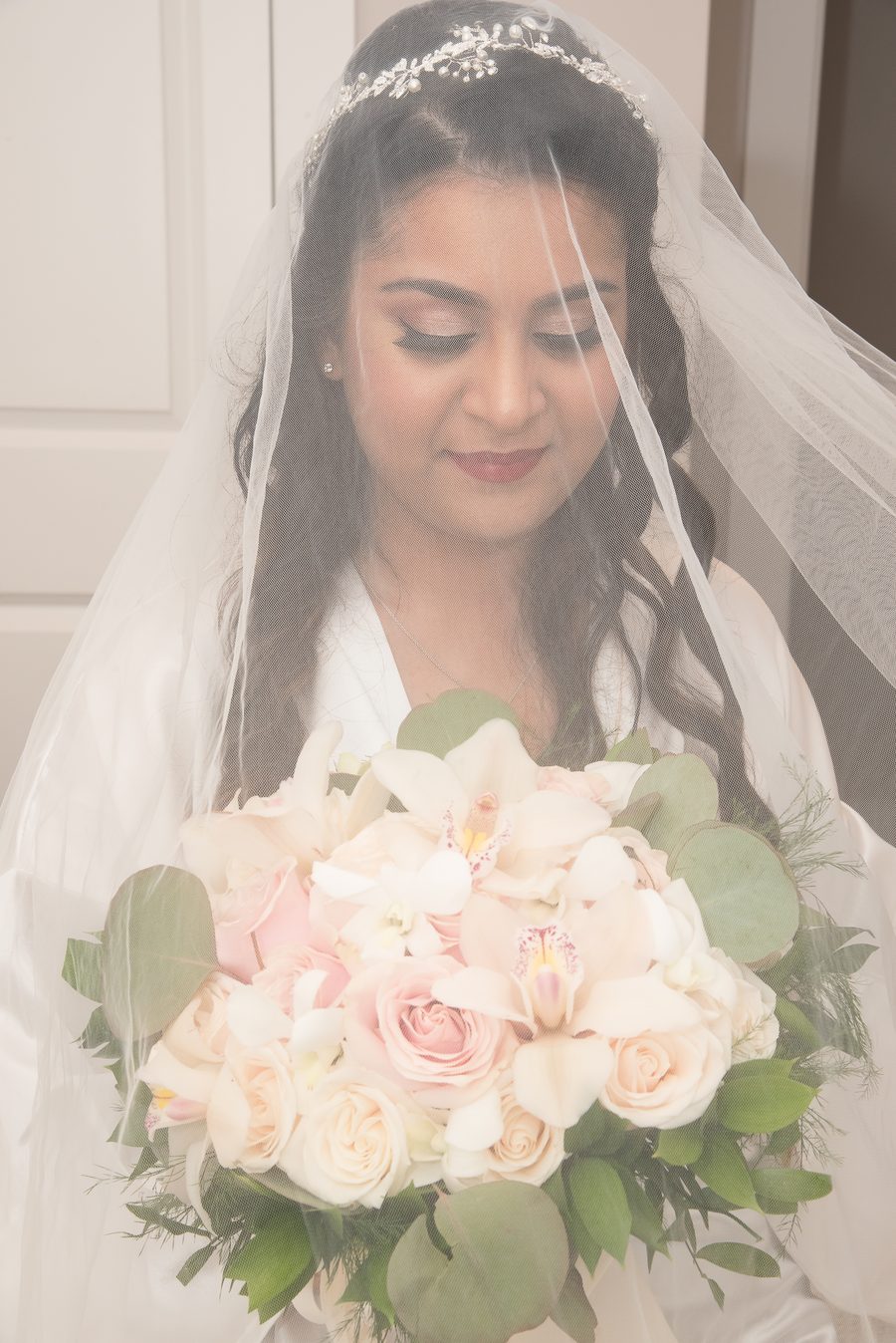 Bride beneath her veil holding a blush rose bouquet